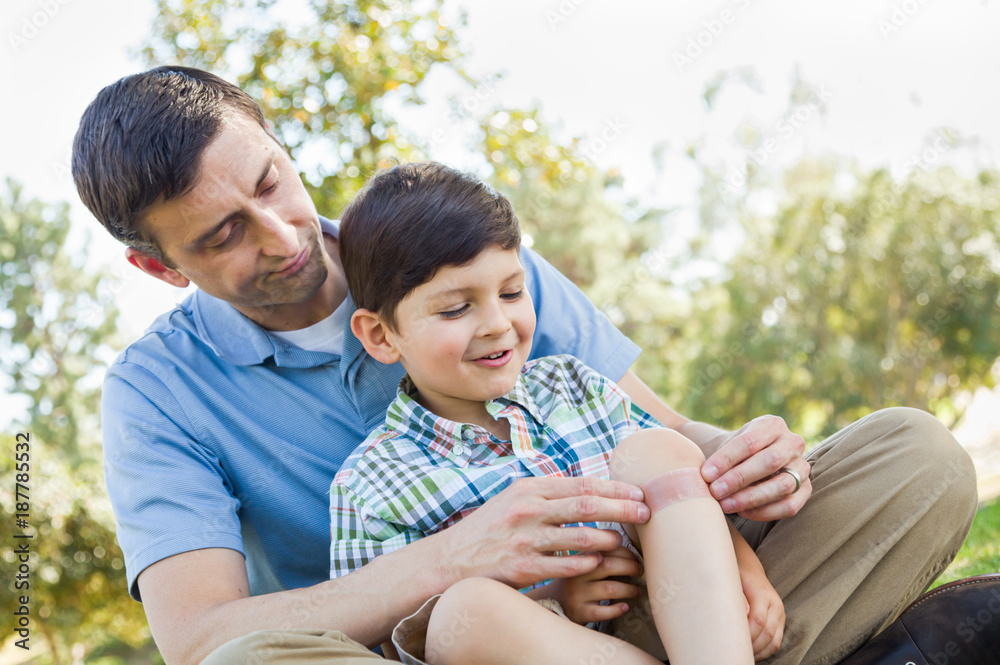 Loving Father Puts a Bandage on the Elbow of His Young Son in the Park. Loving Father Puts a Bandage on the Elbow of His Young Son in the Park.