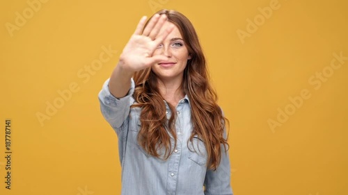 Smiling ginger woman in denim shirt sends air kiss and saying goodbuy while waving at camera and walking away over yellow background photo