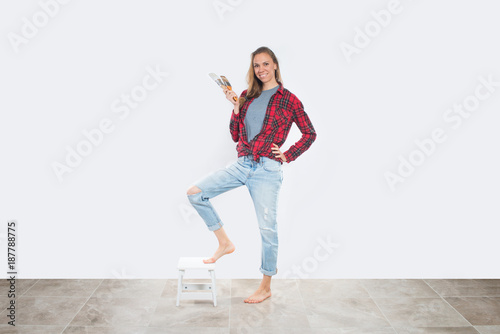 Happy young woman with paintbrushes near empty wall