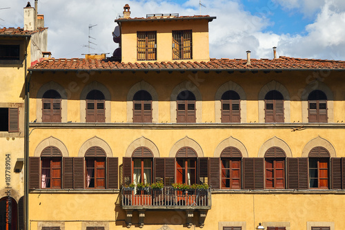 Part of the facade of an old Italian building in Florence with arched windows and balcony