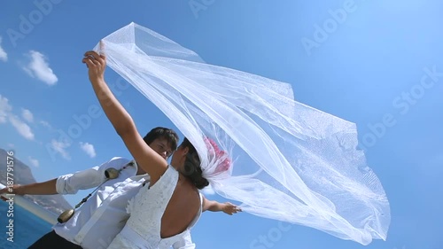 bride and groom stand on a strong wind at the wedding day near the sea. Veil brides beautifully fluttering in the wind. Greece.