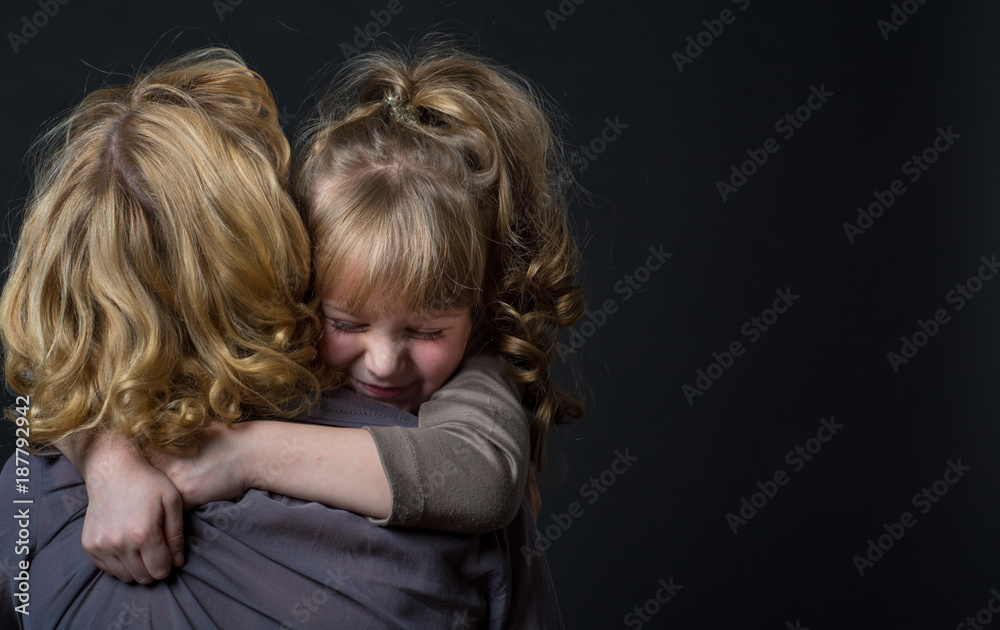 Photo shooting indoors. On a black background. Child ( girl ) hugs his mother.
