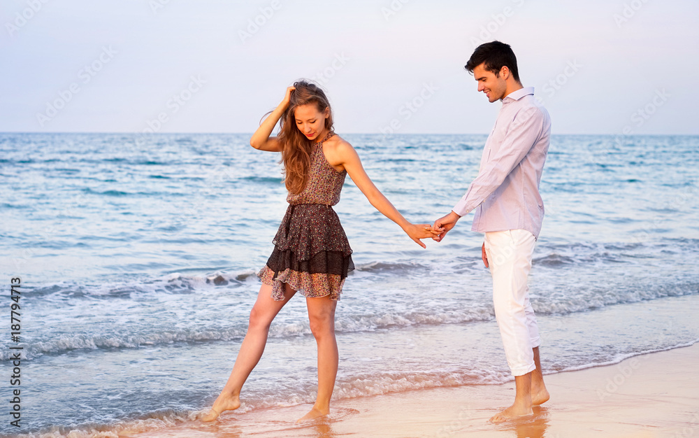  Young couple walking at sunset on the beach - Happy lovers holding hands relaxing by the ocean -  Romantic concept of holidays in hot countries