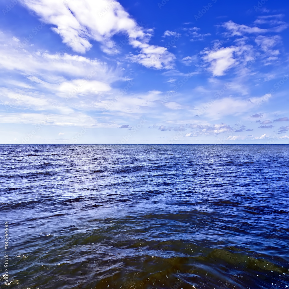 Obraz premium Beautiful dark waves on the horizon with white cumulus clouds in the blue sky, square frame, copy space for text. Abstract seascape on a summer sunny day on Black Sea, Sochi, Russia.