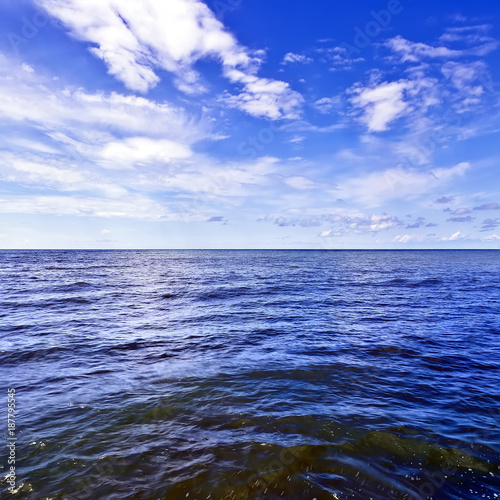 Beautiful dark waves on the horizon with white cumulus clouds in the blue sky, square frame, copy space for text. Abstract seascape on a summer sunny day on Black Sea, Sochi, Russia.