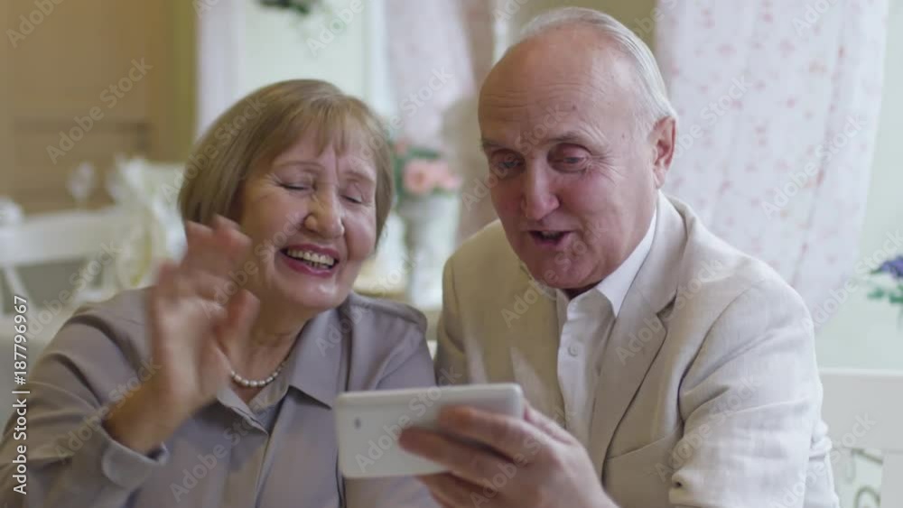 Medium shot of happy senior woman and man sitting in cafe and chatting with family over video call on mobile phone Medium shot of happy senior woman and man sitting in cafe and chatting with family over video call on mobile phone