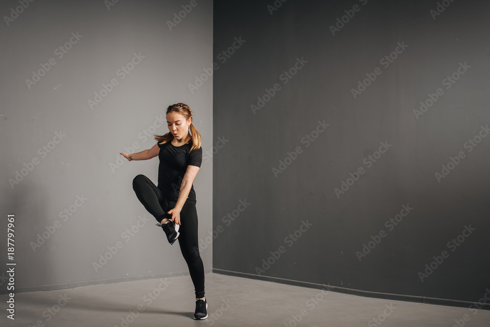 Fitness runner woman doing warm-up routine in gym, stretching leg muscles with standing single knee to chest stretch. Female athlete preparing legs for cardio workout in sportswear. Fitness runner woman doing warm-up routine in gym, stretching leg muscles with standing single knee to chest stretch. Female athlete preparing legs for cardio workout in sportswear.