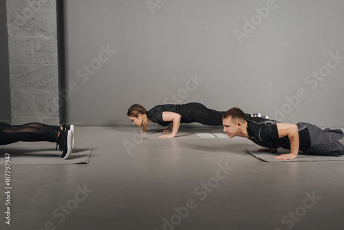 Group of people doing straight arm plank in gym. Young attractive people practicing yoga lesson. Side view of sportsmans doing planking exercise. Concept of healthy. Selective focus.