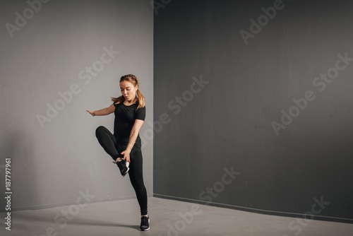 Fitness runner woman doing warm-up routine in gym, stretching leg muscles with standing single knee to chest stretch. Female athlete preparing legs for cardio workout in sportswear.