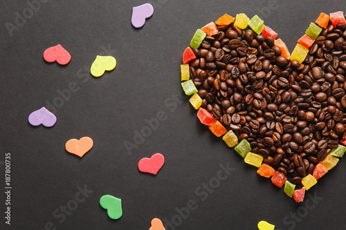 Colorful paper, candied fruits in the form of heart, brown coffee beans isolated on black background for design. Saint Valentine's Day card, fabruary 14, holiday concept. Copy space for advertisement.