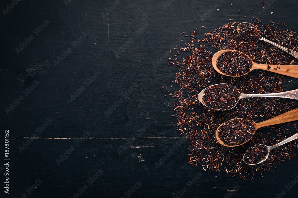 Black wild dry rice on a spoon. On a wooden background. Top view. Copy space.
