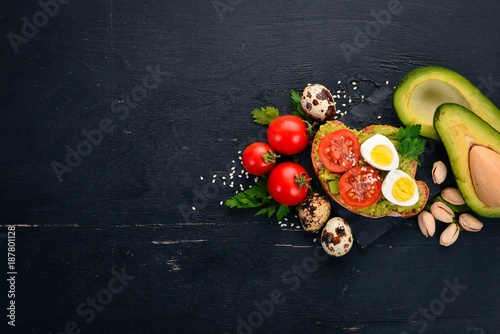 Sandwich with quail eggs, avocados, cherry tomatoes and pistachios. On a wooden background. Top view. Free space for your text.