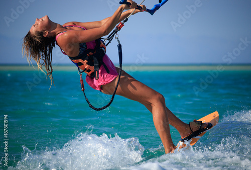 Kite surfing girl in sexy swimsuit with kite in sky on board in blue sea riding waves with water splash. Recreational activity, water sports, action, hobby and fun in summer time. Kiteboarding sport