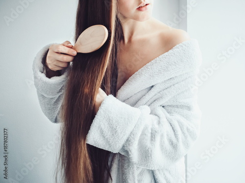 Fotografie, Obraz Cute, young woman in a soft, terry dressing gown, combing her hair after Spa Ser