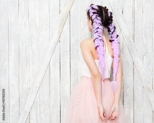 A young girl in a light outfit with her hands behind her back. Hairstyle with colored braids. Close-up. photo