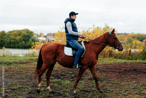 man learns riding a horse in autumn in a rural landscape © ShevarevAlex