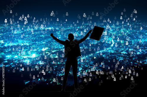 silhouette of businessman with document bag in hand raise arms up because success in business over night city with people icon background