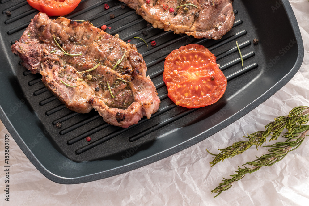 Grilled steak on grill pan with tomatoes and lemon on white background Grilled steak on grill pan with tomatoes and lemon on white background