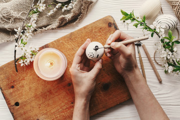 hand painting modern easter egg top view. preparation for holiday, easter celebration. stylish  painted egg. process of coloring eggs with wax and candle. family traditions. flat lay