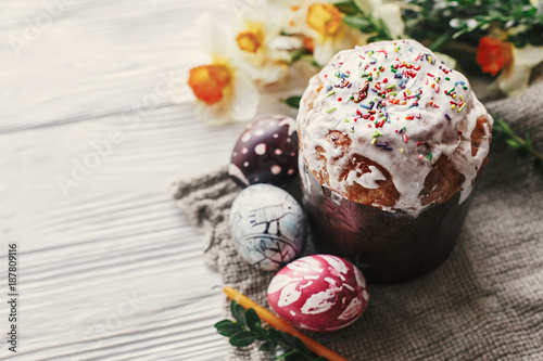 stylish easter bread and painted eggs on rustic wooden background with candle yellow flowers and greenery. happy easter, greeting card. space for text