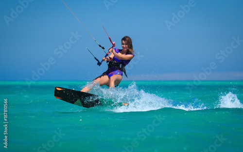 Kite surfing girl in sexy swimsuit with kite in sky on board in blue sea riding waves with water splash. Recreational activity, water sports, action, hobby and fun in summer time. Kiteboarding sport
