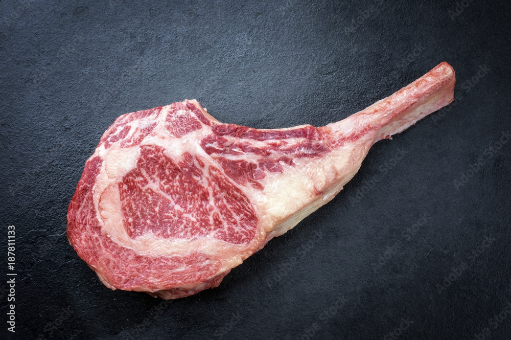 Raw dry aged wagyu tomahawk steak as close-up on black board