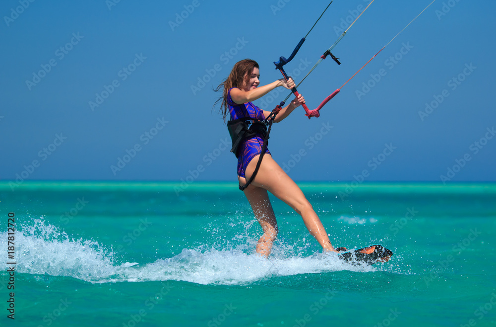 Kite surfing girl in sexy swimsuit with kite in sky on board in blue sea  riding