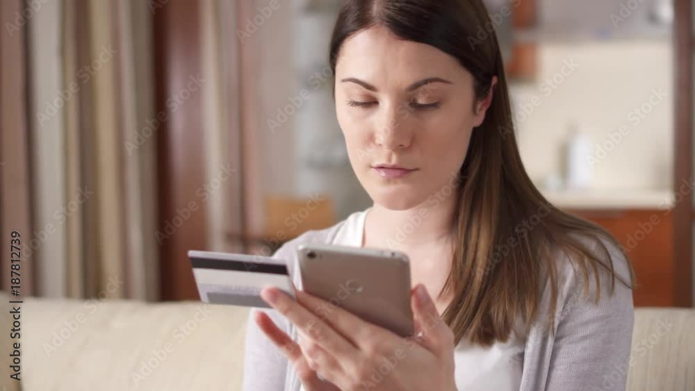 Smiling businesswoman shopaholic sitting on sofa in living room buying online with credit card on mobile phone. Consumerism internet online purchases Smiling businesswoman shopaholic sitting on sofa in living room buying online with credit card on mobile phone. Consumerism internet online purchases