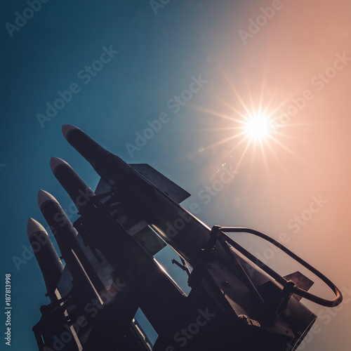 Four rockets of anti-aircraft missile system are directed upwards against the background of blue sky and sun at sunset