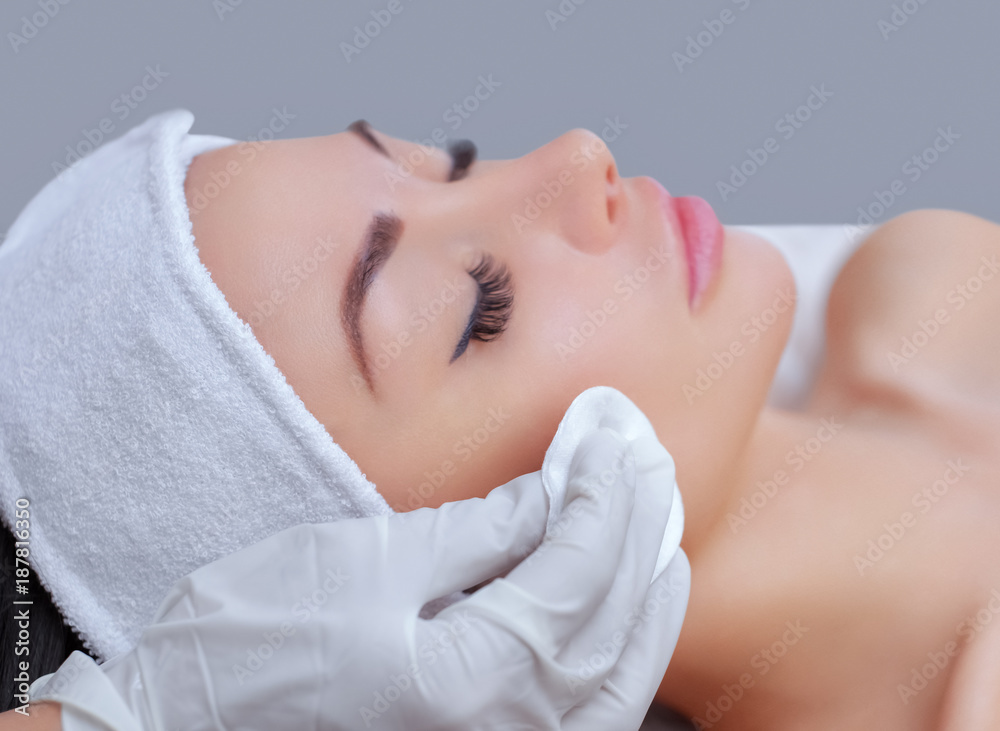 The doctor cosmetologist cleanses with a tonic the face skin of a beautiful, young woman in a beauty salon.Cosmetology skin care. The doctor cosmetologist cleanses with a tonic the face skin of a beautiful, young woman in a beauty salon.Cosmetology skin care.