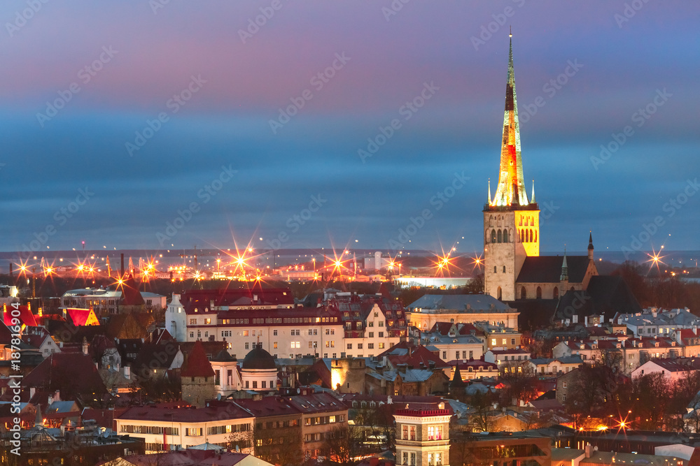 Aerial cityscape with Medieval Old Town illuminated in evening twilight and St. Olaf Baptist Church, sea and port in Tallinn, Estonia