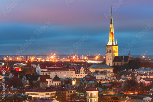 Aerial cityscape with Medieval Old Town illuminated in evening twilight and St. Olaf Baptist Church  sea and port in Tallinn  Estonia