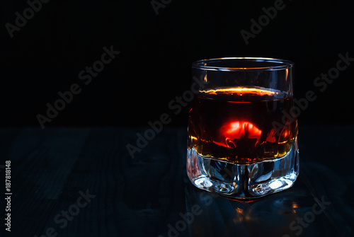 A glass of whiskey on a black background and a wooden table
