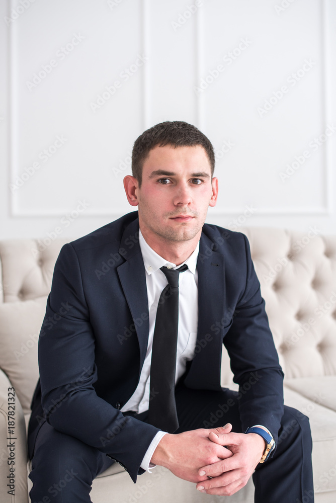 Portrait of a young serious and confident man in a suit sitting on the couch and looking at camera. Portrait of a young serious and confident man in a suit sitting on the couch and looking at camera.