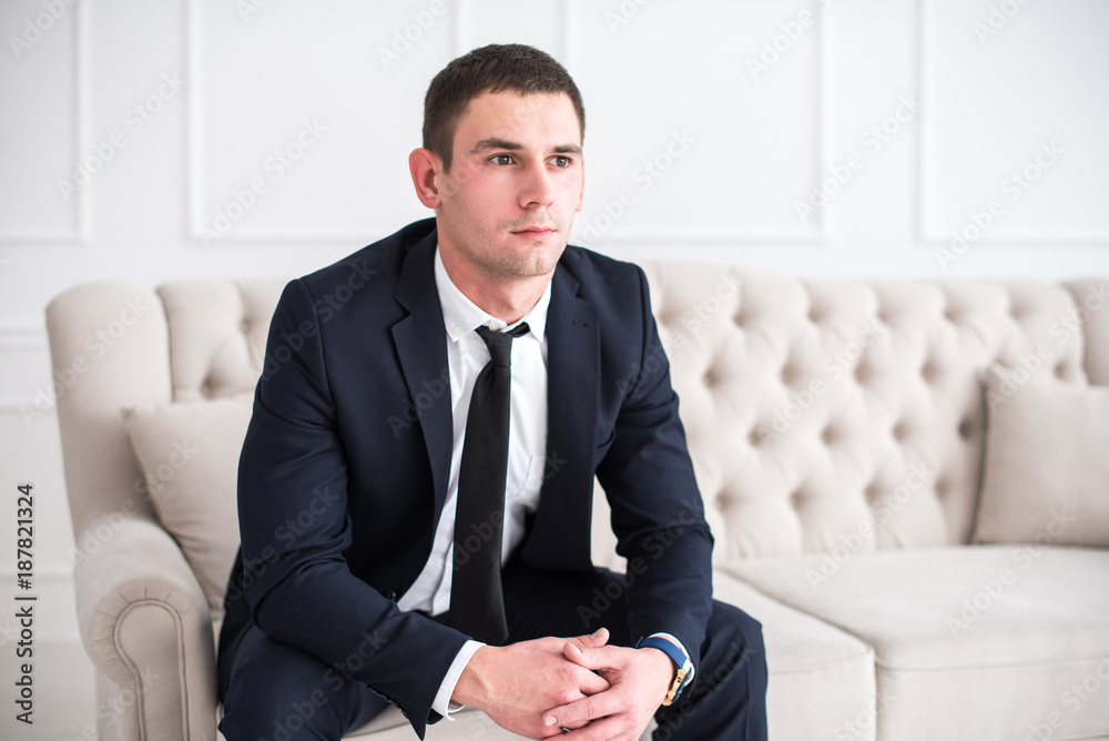 Fototapeta premium Young serious and confident man in a business suit sitting on the couch