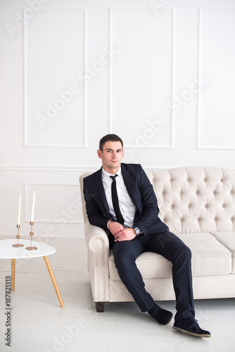 Portrait of a young serious and confident man in a suit sitting on the couch and looking at camera. photo