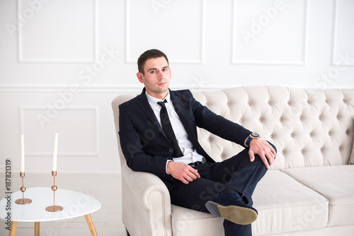 Portrait of a young serious and confident man in a suit sitting on the couch and looking at camera. photo