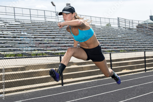 Cute and fit young teen Caucasian girl working out on outdoor track leaps in the air (hurdles)
