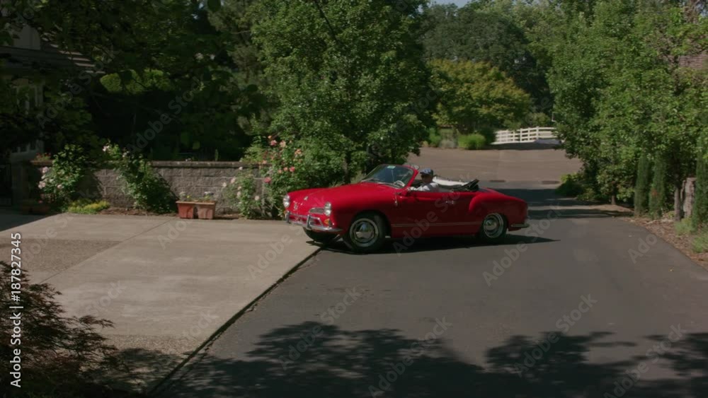 Tracking shot of man pulling out of driveway in classic convertible car.  Fully released for commercial use