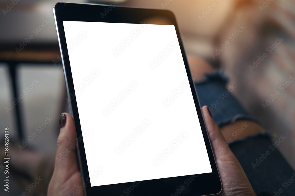 Mockup image of a woman wearing ripped jean sitting cross legged , holding black tablet pc with blank white desktop screen on thigh in cafe Mockup image of a woman wearing ripped jean sitting cross legged , holding black tablet pc with blank white desktop screen on thigh in cafe