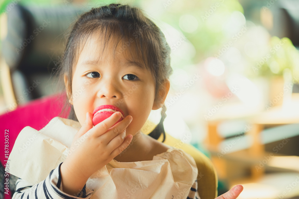 Little asian girl eating macaron in restaurant. Little asian girl eating macaron in restaurant.