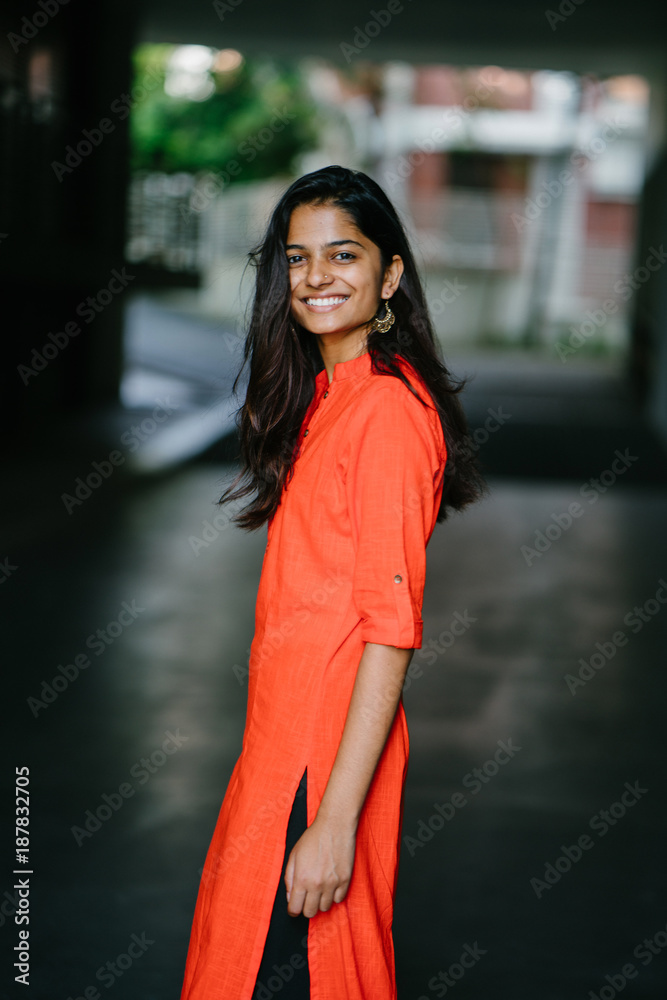 Portrait of attractive and young Indian woman smiling in an orange ethnic dress during the day