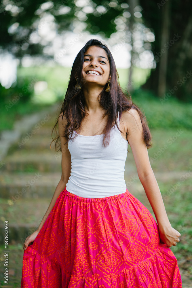 Candid portrait of a young and attractive Indian Asian woman in a lush, green park (Fort Canning Park in Singapore) on a sunny day. She is dressed in a fashionable, casual summer outfit. Candid portrait of a young and attractive Indian Asian woman in a lush, green park (Fort Canning Park in Singapore) on a sunny day. She is dressed in a fashionable, casual summer outfit.