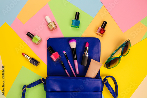 Things from open lady purse. Cosmetics and women's accessories fell out of blue handbag on colourful background. Top view. 