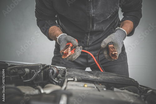 Obraz na płótnie Car mechanic hands in gloves working with booster jumper cables and charging a discharged battery in the garage