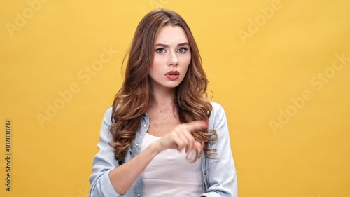 Serious Pensive brunette woman in denim shirt looking around and showing silence gesture over yellow background photo