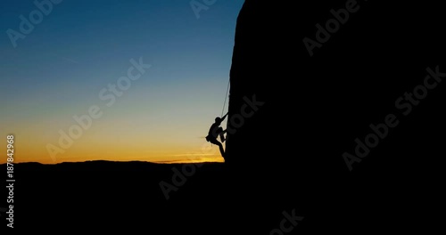 Aerial - Silhouette of a man rock climbing in the evening light.
