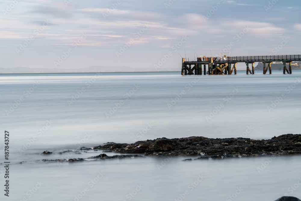 Looking across the Bay to Fishermen on Cornwallis Wharf on a Summer Evening in Auckland New Zealand - Long Exposure Looking across the Bay to Fishermen on Cornwallis Wharf on a Summer Evening in Auckland New Zealand - Long Exposure
