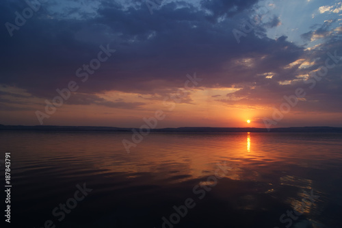 Sunset over the river. The sun in the clouds sits across the river. Pink sunset and clouds over the water.