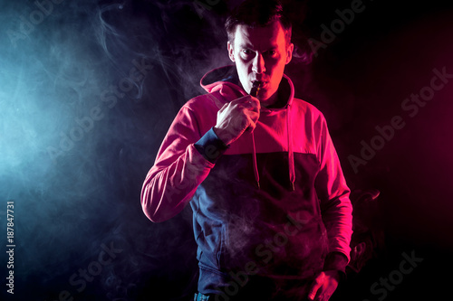 The man smoke an electronic cigarette, vape on a background of red and white smoke